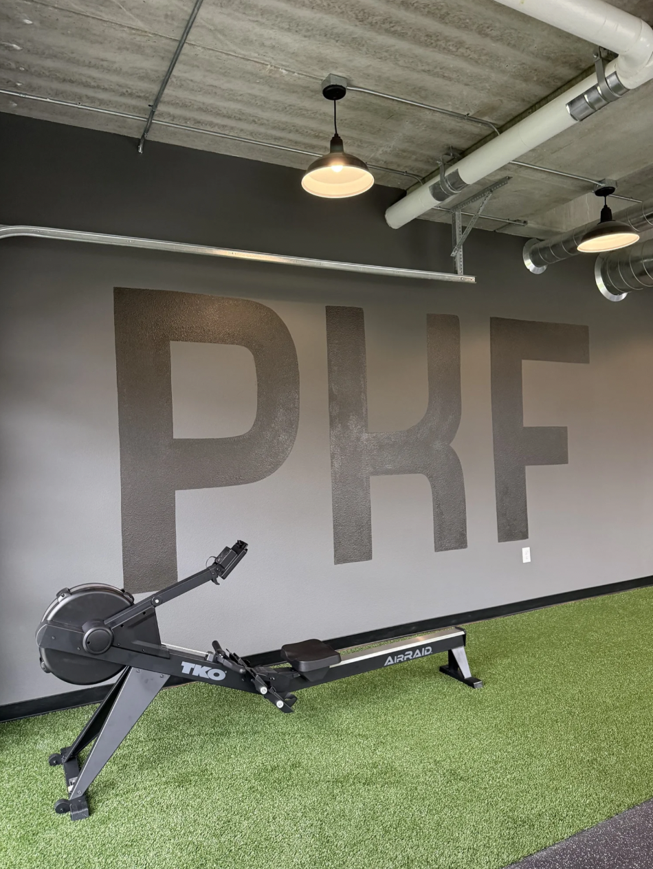 A rowing machine on the green turf beneath the PKF wall lettering at Wausau