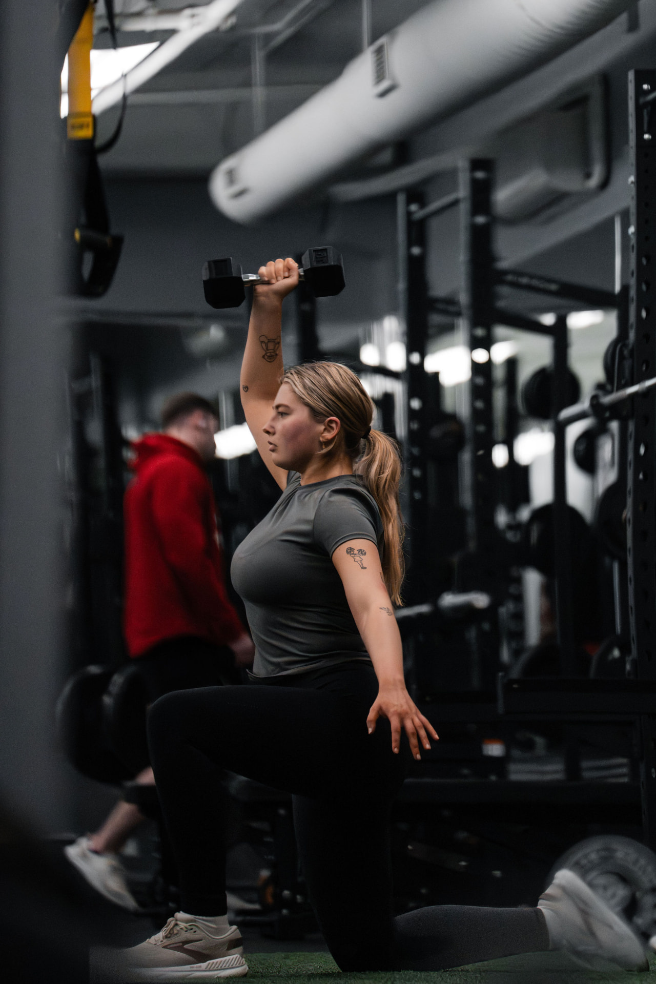 A PKFit member performing a kneeling overhead dumbbell press