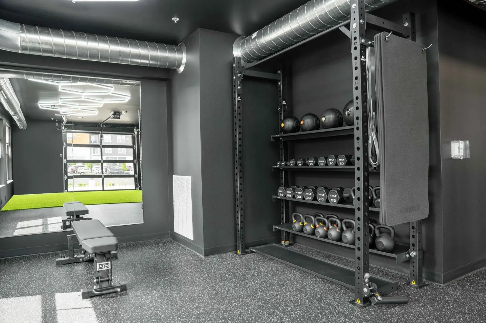 The training rig with mats and dumbbells at PKFit Verona, opening to the outdoor turf