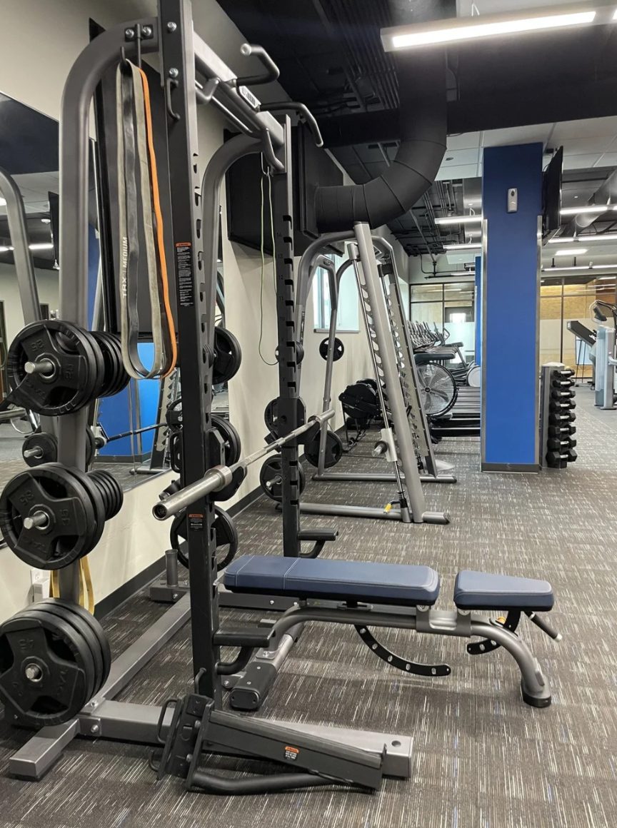 A barbell rack and adjustable bench beside the Smith machine at PKFit Madison East