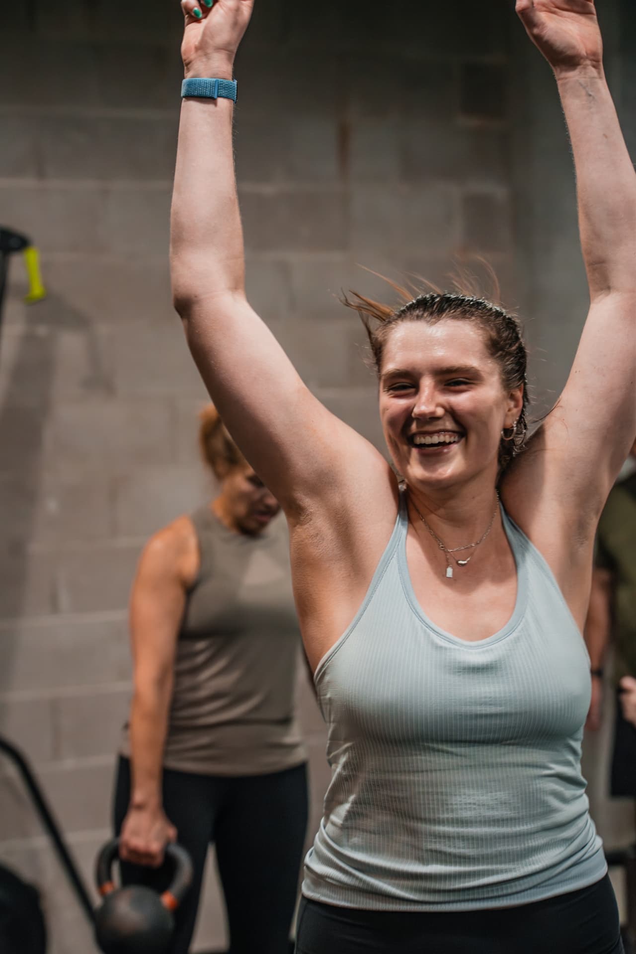 A smiling member raising her arms after a set during a PKFit class