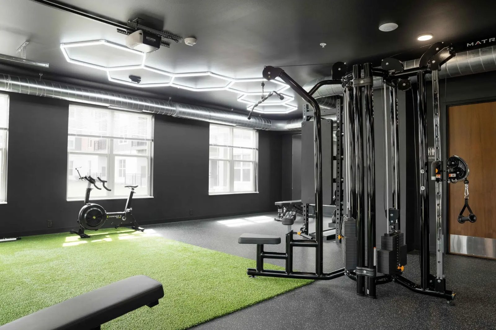 The indoor turf at PKFit Verona with hexagonal ceiling lights and a stationary bike