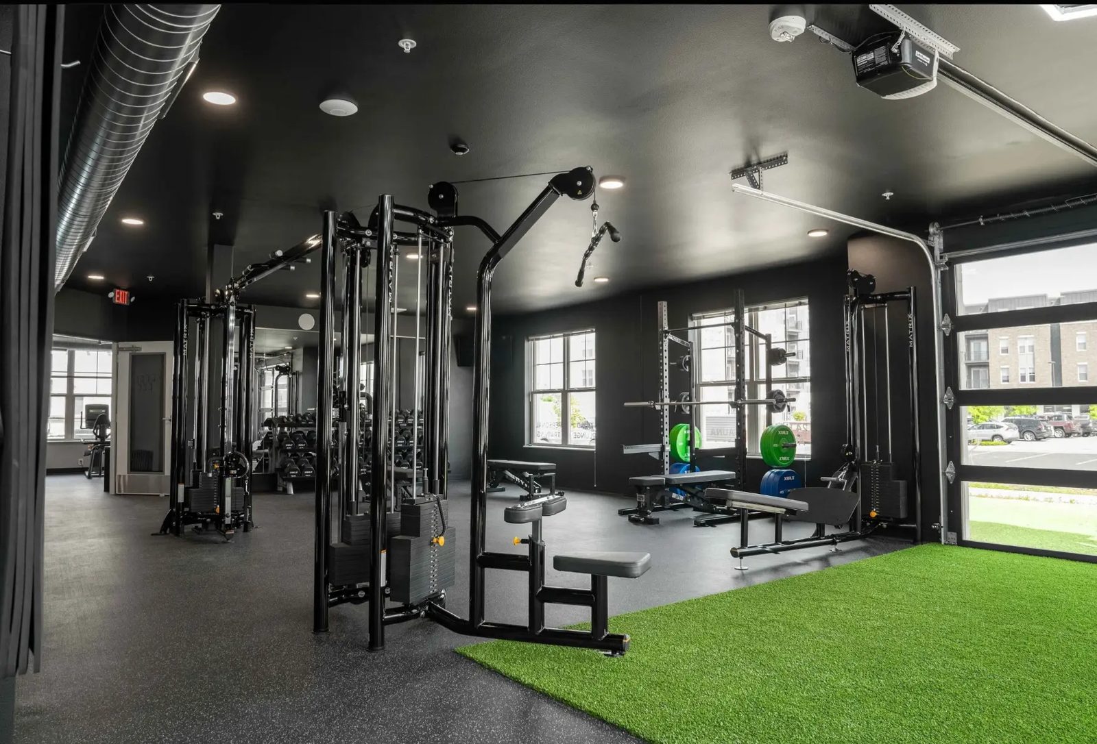 The PKFit Verona strength area with Matrix cable machines, a squat rack, and the open glass garage door