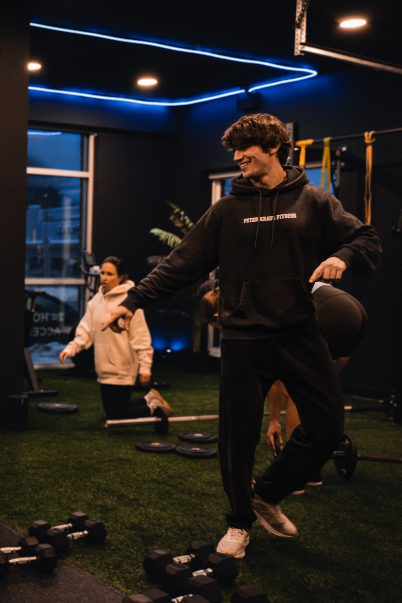 A member in PKFit gear moving across the gym turf during a training session