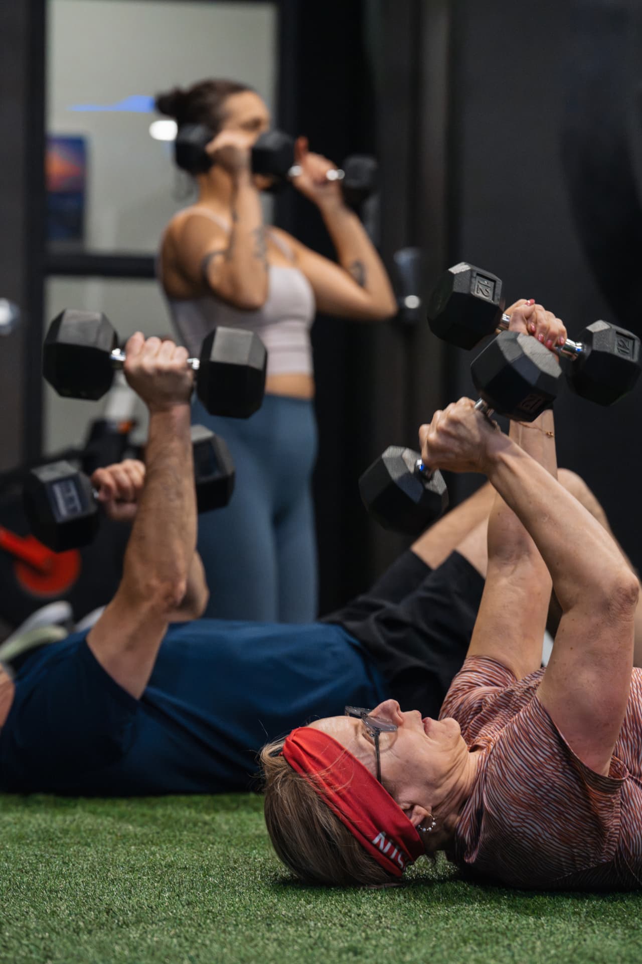 Members doing dumbbell floor presses on the turf during a group strength class