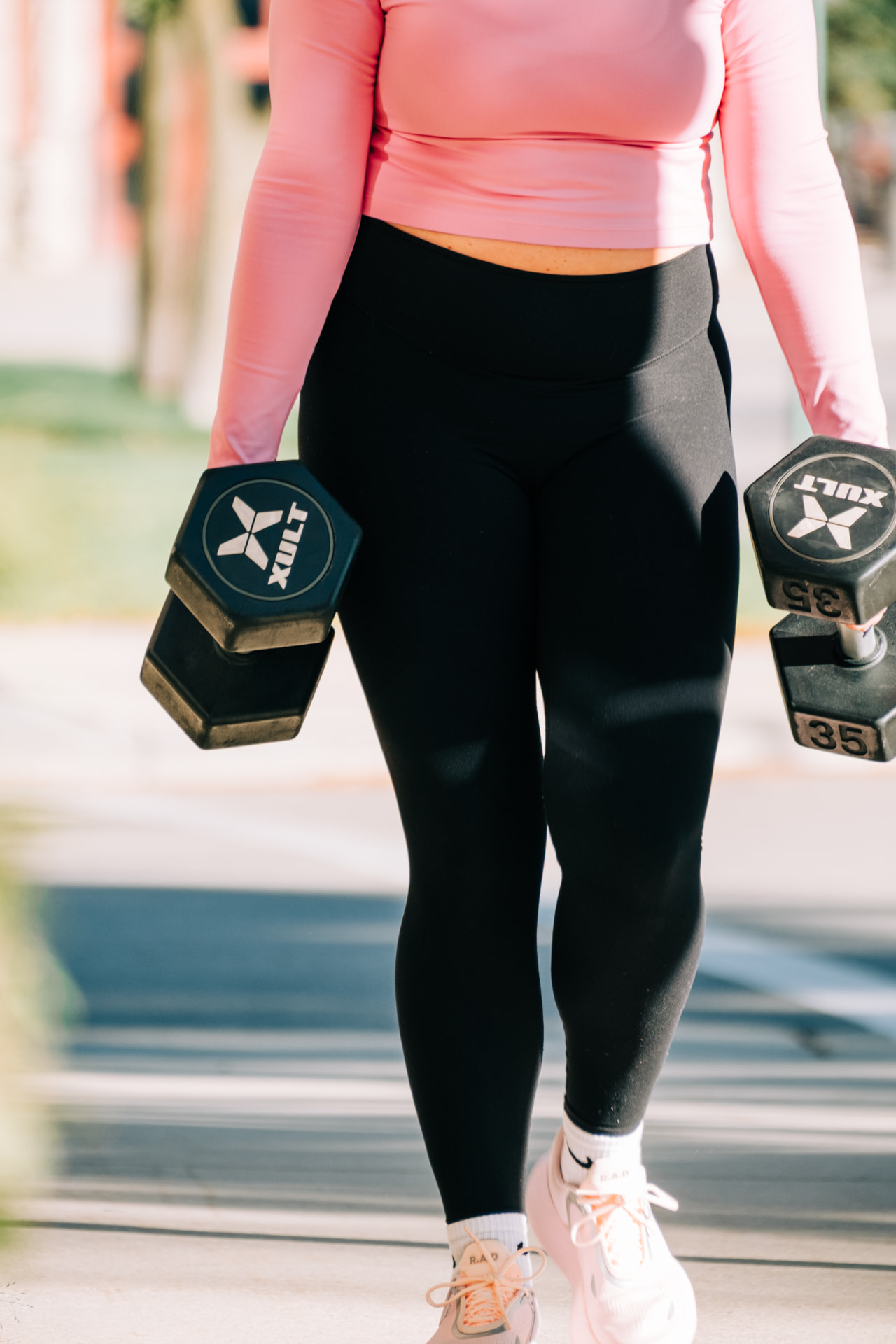 A person walking outdoors carrying a dumbbell in each hand